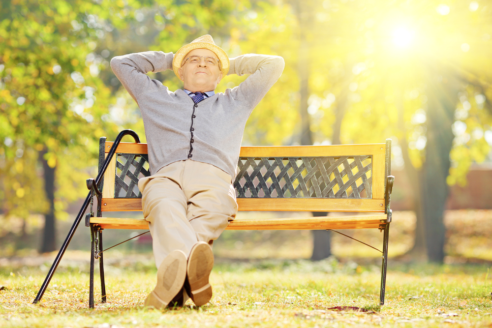 Older man sitting on a bench while basking in the sun.